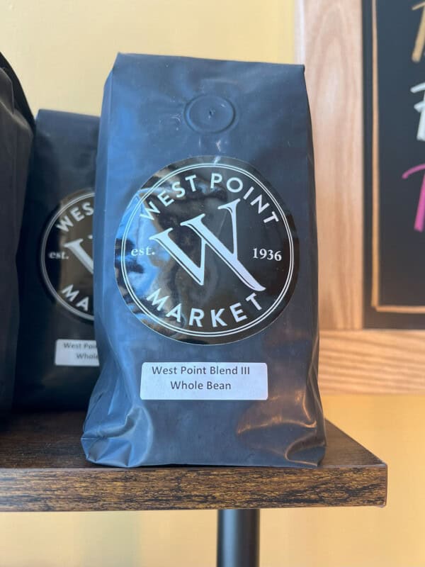 A bag of WPM Original Coffee Blends whole bean coffee rests on a wooden shelf, featuring a circular black and white logo on the front of its packaging.