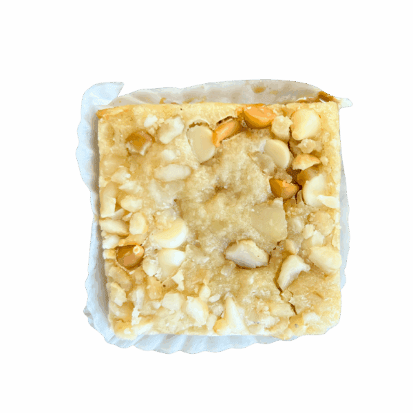 A square WPM Original Triple Layer Brownie topped with chopped macadamia nuts sits on a crinkled white paper liner against a plain white background.