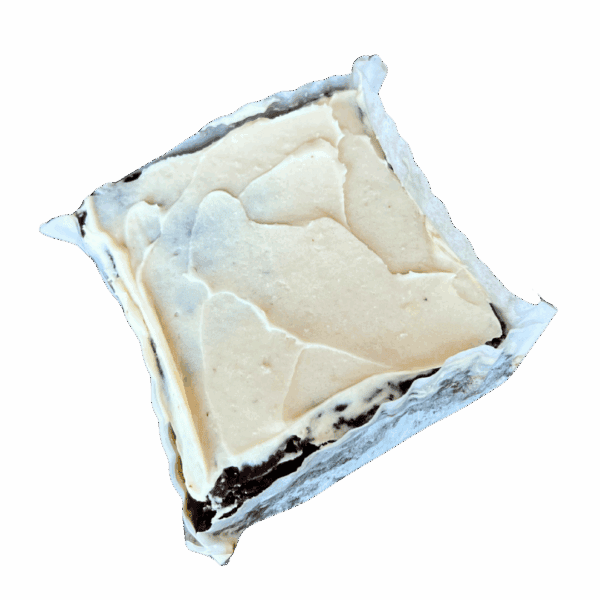 A square WPM Original Triple Layer Brownie with white frosting on top, partially wrapped in parchment paper, displayed on a plain white background.
