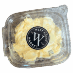 A clear plastic container filled with egg salad, topped with a black and white West Point Market label on the lid. The salad contains chopped eggs, mayonnaise, and green onions.