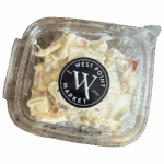 A clear plastic container labeled West Point Market holds a creamy salad with chunks of pasta, red bell pepper, and green vegetable pieces. The lid is closed and the background is white.