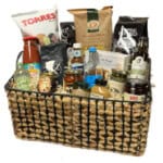 The Gift Basket - Medium features a woven basket filled with an assortment of gourmet chips, sauces, bottled drinks, jars, and snack packages, perfectly arranged for a delightful hamper.