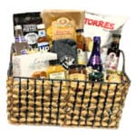The Gift Basket - Medium features a woven basket filled with chips, pretzels, sauces, bottled drinks, and jars—all neatly arranged for a perfect gift presentation.